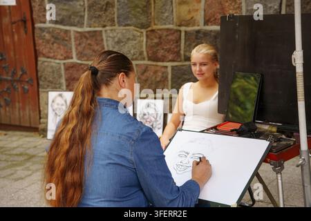 Sopot, Pologne – 25 juillet 2026 : Artiste de rue esquissant le portrait d'une jeune femme sur un tableau blanc en extérieur, mettant en valeur un talent artistique en direct et un service public Banque D'Images