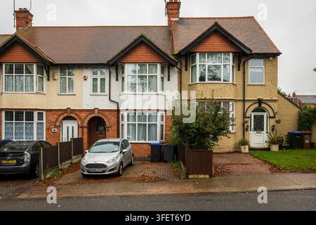 Deux maisons mitoyennes de banlieue à Northampton, Royaume-Uni, présentant des façades en brique et en stuc, des baies vitrées, des allées avec des voitures garées, des jardins avant, des poubelles a Banque D'Images