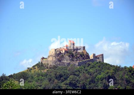 Forteresse médiévale de Rupea dressée au sommet d'une colline de basalte au-dessus d'arbres verts sous un ciel bleu nuageux, Rupea, Transylvanie, Roumanie. Banque D'Images