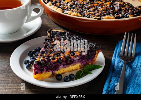 Tranche de tarte aux myrtilles faite maison avec des fruits frais et du thé. Tranche de délicieuse tarte aux myrtilles servie sur une assiette blanche avec des fruits frais et de la menthe à côté Banque D'Images