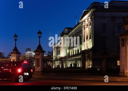 Un taxi passe devant le palais de Buckingham, le siège administratif et la résidence royale du monarque britannique à Londres, illuminé la nuit. Banque D'Images