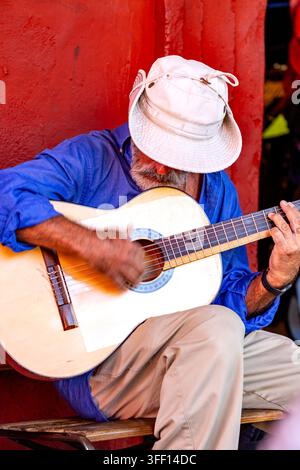 SAN MIGUEL DE ALLENDE, MEXIQUE – 1ER NOVEMBRE 2019 : Un homme barbu et chapeauté joue de la guitare devant un mur rouge. L'homme porte une chemise bleue Banque D'Images