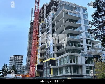 Un immeuble d'appartements modern de grande hauteur en construction, présentant une grue rouge imposante et des balcons en verre incurvés élégants contre un ciel nuageux Banque D'Images