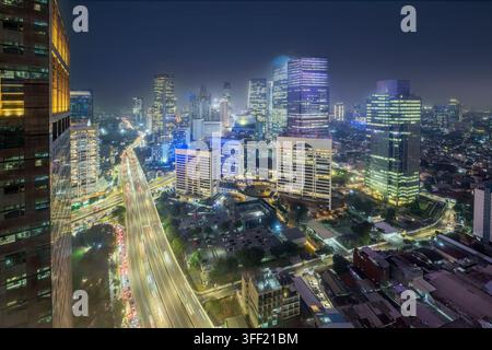 Vue aérienne nocturne des gratte-ciel illuminés et de la circulation intense sur une autoroute principale du quartier des affaires central de Jakarta, Indonésie. Paysages urbains ba Banque D'Images