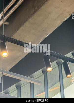 Intérieur industriel moderne avec béton apparent, panneaux acoustiques noirs au plafond, cadre métallique, fenêtres en verre et éclairage linéaire chaud, créant Banque D'Images