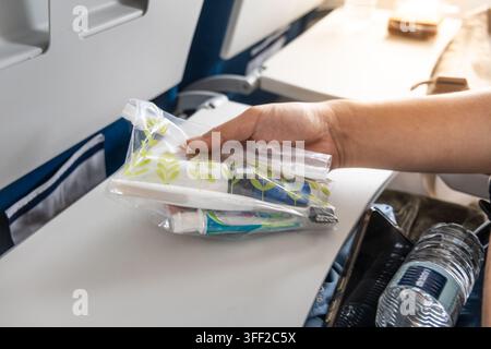 Person tenant des produits essentiels de soins personnels dans un sac en plastique transparent dans la cabine d'avion, destinés au rafraîchissement en vol pendant un vol long-courrier. Banque D'Images