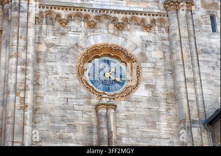 Un plan rapproché détaillé révèle une horloge circulaire ornée avec des chiffres romains et des aiguilles dorées, magnifiquement intégrée dans la façade en pierre érodée Banque D'Images