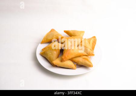 Une vue de dessus d'une assiette de samosas triangulaires dorés à point disposés sur un fond blanc immaculé. Les pâtisseries frites et croustillantes sont présentées de manière simple Banque D'Images