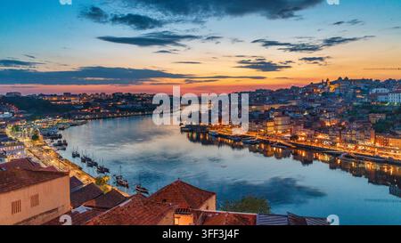 Vue panoramique de Porto, Portugal, au crépuscule, montrant le quartier illuminé de Ribeira et les bateaux traditionnels se reflétant dans le fleuve Douro Banque D'Images