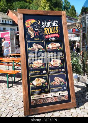 Bad Herrenalb, Allemagne, le 05 septembre 2026 Panneau en bois affichant divers wraps et sandwichs roulés garnis sur un marché de rue ensoleillé, avec pavé Banque D'Images