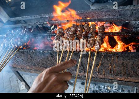 Chef faisant griller de la viande de chèvre Sate Klatak indonésienne sur des brochettes métalliques au-dessus du charbon de bois enflammé, nourriture de rue authentique de Yogyakarta. Banque D'Images