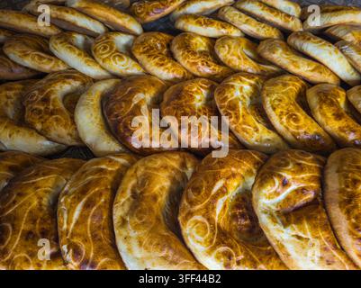 Vue rapprochée d'une variété de pain fraîchement cuit mettant en valeur des croûtes dorées et des motifs uniques. L'assortiment comprend à la fois des pains plats et des pains ronds, soulignant les techniques de boulangerie traditionnelles. Banque D'Images
