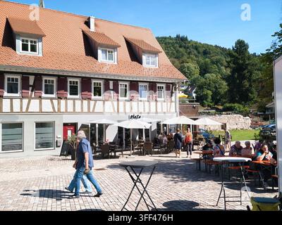 Bad Herrenalb, Allemagne, 5 septembre 2026 : Terrasse extérieure d’un café à côté d’une maison à colombages avec des habitants assis et marchant sur la place pavée, wh Banque D'Images