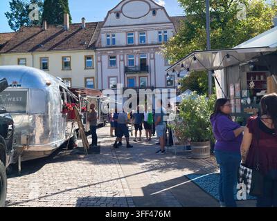 Bad Herrenalb, Allemagne, 5 septembre 2026 : Marché de rue ensoleillé sur une place historique montrant des camions-restaurants, des clients en train de regarder, des guirlandes lumineuses, pavé Banque D'Images