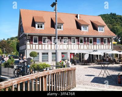 Bad Herrenalb, Allemagne, 5 septembre 2026 Bâtiment à colombages inondé de lumière avec toit de tuiles abrupt à côté des sièges extérieurs d'un café, avec rue, place, square, Banque D'Images