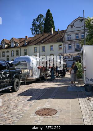 Bad Herrenalb, Allemagne, le 5 septembre 2026 : des camions-restaurants et des visiteurs bordent une rue pavée près d’anciens bâtiments européens sous un ciel bleu clair, créant une ambiance vivante Banque D'Images