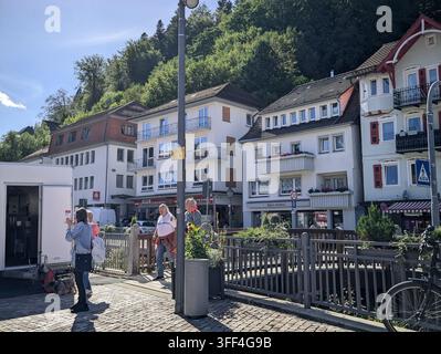 Bad Herrenalb, Allemagne, 5 septembre 2026 Rue en pente ensoleillée dans une ville européenne avec des appartements blancs, des devantures de magasins, un trottoir en pavés, des panneaux de signalisation, r Banque D'Images