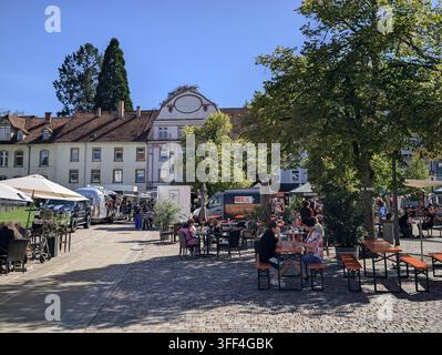 Bad Herrenalb, Allemagne, 5 septembre 2026 : Des tables d’extérieur et des camions de restauration remplissent la place pavée à côté de façades historiques et de grands arbres, avec rue, fo Banque D'Images