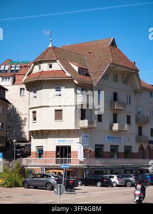 Bad Herrenalb, Allemagne, 5 septembre 2026 : Bâtiment résidentiel urbain ensoleillé avec toit pentu en tuiles, façade crème, petits balcons et voitures garées à côté Banque D'Images