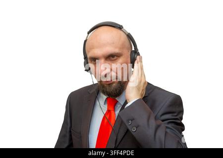 Un homme d'affaires chauve en costume écoute à travers des écouteurs tout en ajustant l'oreillette sur un fond blanc. Banque D'Images