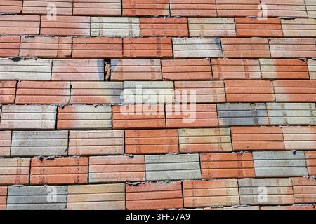 un mur de maçonnerie inachevé construit avec des briques de terre cuite multicolores rainurées horizontalement et des joints de mortier apparents. Banque D'Images