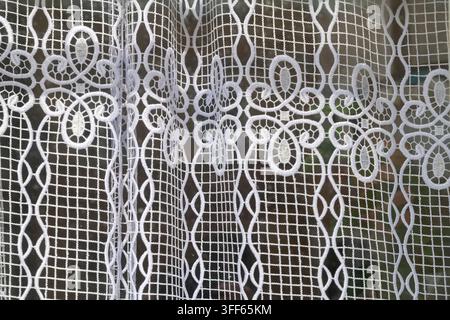 Rideau en dentelle blanche avec des motifs floraux délicats suspendu devant une fenêtre. Banque D'Images