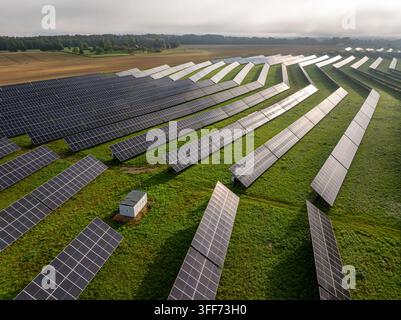Vue aérienne par drone d'une ferme photovoltaïque solaire avec des rangées de panneaux dans un paysage rural verdoyant Banque D'Images