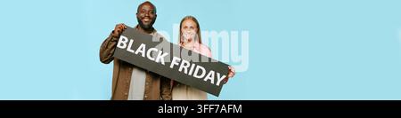 Portrait en tête d’un homme mature afro-américain souriant et d’une jeune femme caucasienne tenant un panneau Black Friday. Image adaptée au marketing de détail Banque D'Images