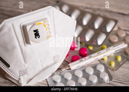 Close up d'un masque de protection N95 à côté de pilules médicinales colorées dans des plaquettes unitaires et d'un thermomètre médical, représentant la protection contre le coronavirus, épi grippal Banque D'Images