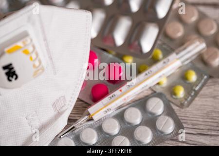 Close up d'un masque de protection N95 à côté de pilules médicinales colorées dans des plaquettes unitaires et d'un thermomètre médical, représentant la protection contre le coronavirus, épi grippal Banque D'Images
