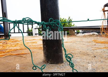 Un nœud de corde verte poteau en bois terrasse de sable extérieur corde patinée rambarde plage nautique, noué autour d’un poteau en bois sombre sur une terrasse extérieure de sable à côté de la rambarde Banque D'Images