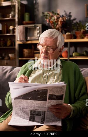 Homme senior concentré portant des lunettes lisant les nouvelles du jour sur un canapé Banque D'Images