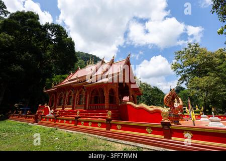 Un temple thaïlandais, temple bouddhiste rouge à l'architecture ornée, forêt tropicale, ciel bleu, nuage blanc, sanctuaire, toit de pagode, lieu sacré avec des détails dorés, lus Banque D'Images