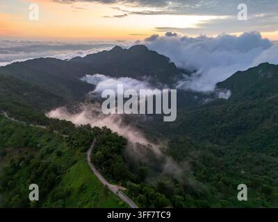 Un paysage montagneux brumeux, route sinueuse, forêt nuageuse, crête au lever du soleil sur une vallée verdoyante avec brouillard, ciel dramatique et scène tranquille des hautes terres du nord Banque D'Images