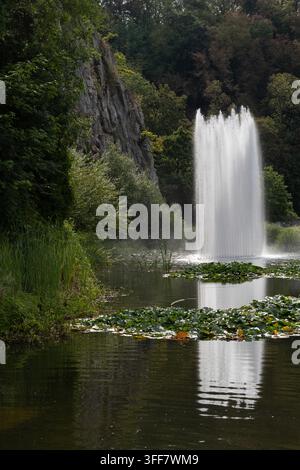 Une haute fontaine s'élève d'un étang tranquille rempli de nénuphars à côté d'une falaise de calcaire et d'une forêt dense à Durbuy en Belgique, créant un Ar pittoresque Banque D'Images