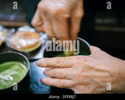 Mains fouettant du thé vert matcha avec un chasen dans un bol dans un café du quartier d'Ukyo, Kyoto, Japon Banque D'Images