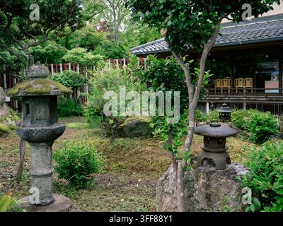 Lanternes en pierre dans un jardin japonais traditionnel avec une végétation luxuriante et un bâtiment en bois, arrondissement d’Ukyo, Kyoto, Japon Banque D'Images