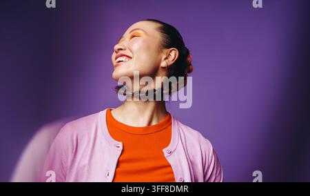 Portrait de beauté asiatique mettant en scène une femme au maquillage audacieux, aux cheveux tressés et à un sourire espiègle, idéal pour les soins de la peau, le bien-être, l'expression de soi et la vitalité Banque D'Images