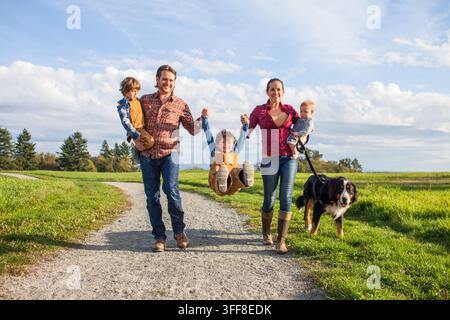 Famille heureuse de cinq personnes avec trois fils promenant leur chien Banque D'Images