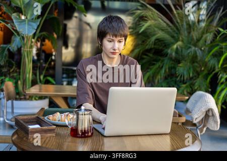 Femme aux cheveux courts travaillant dans un café et semblant absorbée Banque D'Images