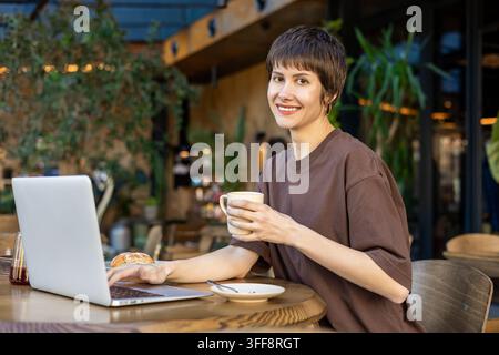 Femme aux cheveux courts travaillant dans un café et semblant absorbée Banque D'Images