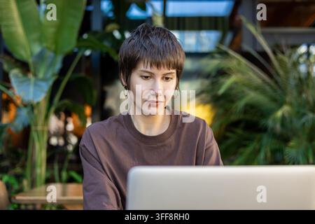 Femme aux cheveux courts travaillant dans un café et semblant absorbée Banque D'Images