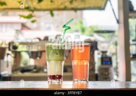 Sélection de boissons servies dans un café-bar, comprenant un verre de bière ambrée, un latte au matcha, un thé glacé et un verre en cours de préparation avec des glaçons. Banque D'Images