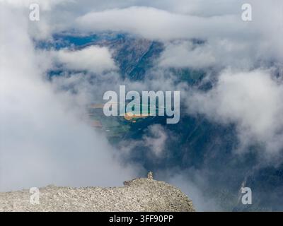 Vue aérienne du sommet du mont Kongen émergeant à travers d'épais nuages avec une vue sur la vallée verdoyante et les champs agricoles en contrebas à Andalsnes, Møre og Banque D'Images