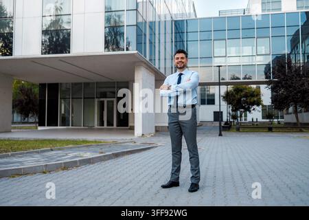 Un homme en chemise blanche et cravate bleue pose devant une structure de bureau contemporaine pendant la journée. Banque D'Images