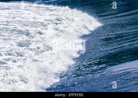 Un cliché d'action dynamique d'une vague de fleuve froide et puissante se brisant sur un barrage structuré, créant un motif épuré d'eau bleu profond et de tourbillons blancs Banque D'Images