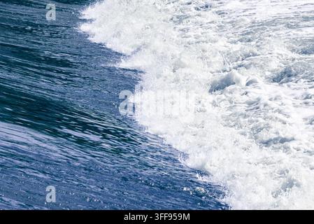Un cliché d'action dynamique d'une vague de fleuve froide et puissante se brisant sur un barrage structuré, créant un motif épuré d'eau bleu profond et de tourbillons blancs Banque D'Images