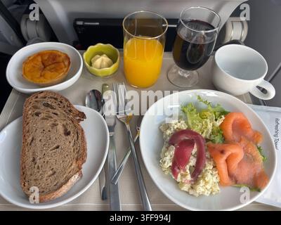 Un dîner de classe affaires en vol servi sur un plateau avec du jus d'orange, du vin rouge, de la salade, du pain de seigle, du beurre et une tarte à la crème traditionnelle portugaise pour de Banque D'Images