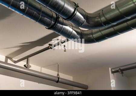 Conduites de ventilation HVAC en métal exposées et tuyaux d'arrosage sur un plafond blanc. Architecture industrielle moderne. Banque D'Images