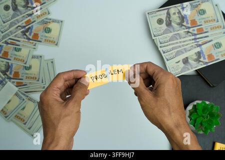 Mains déchirant un billet de papier étiqueté "problème" entouré de billets de dollar américain sur un fond blanc. Banque D'Images